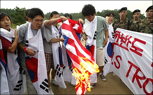 훈련장에 기습적으로 진입한 학생들이 태극기를 몸에 두른 채 미군들이 지켜보는 가운데 성조기를 불태우고 있다. 